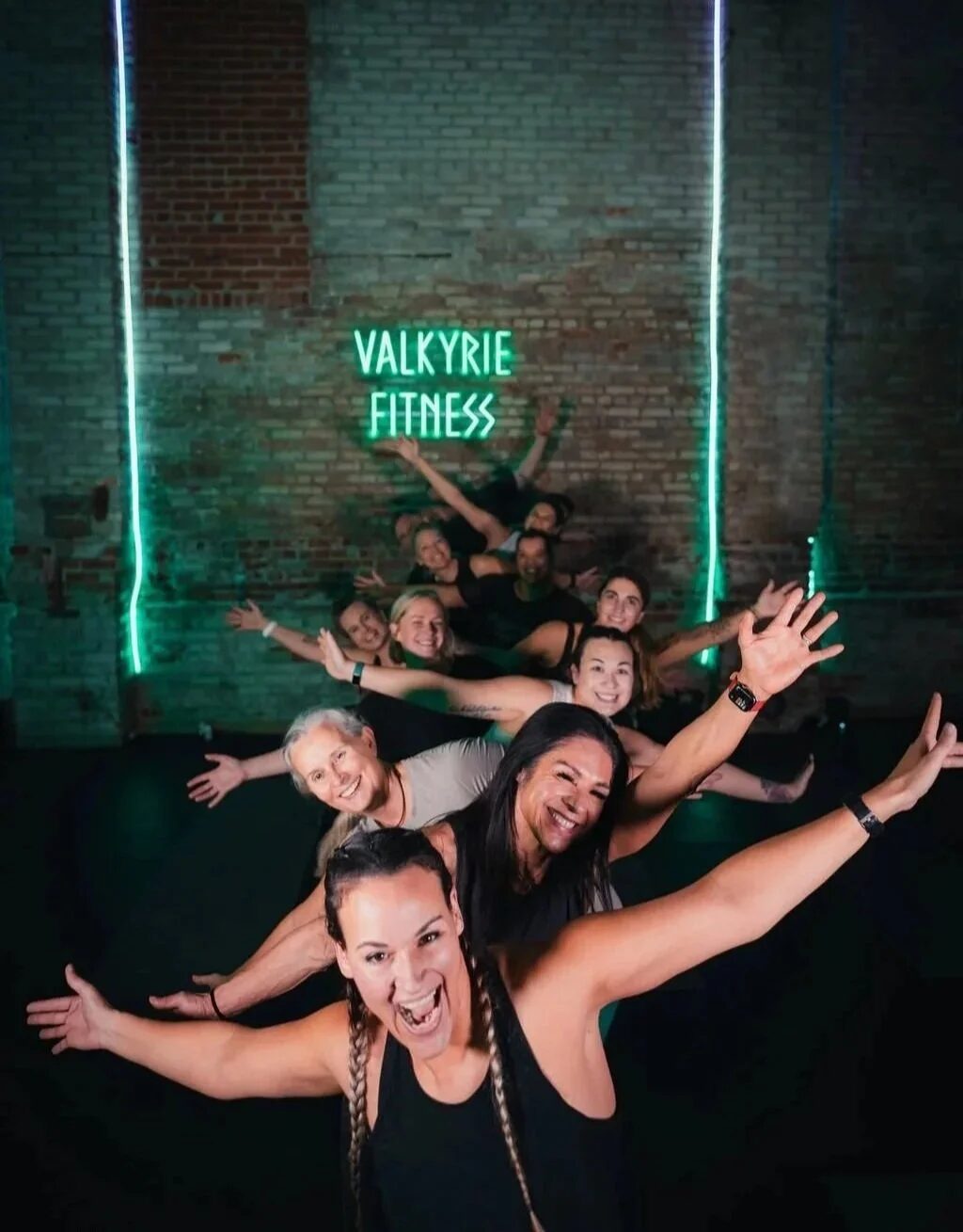 Valkyrie Fitness class members posing under the studio's green neon sign