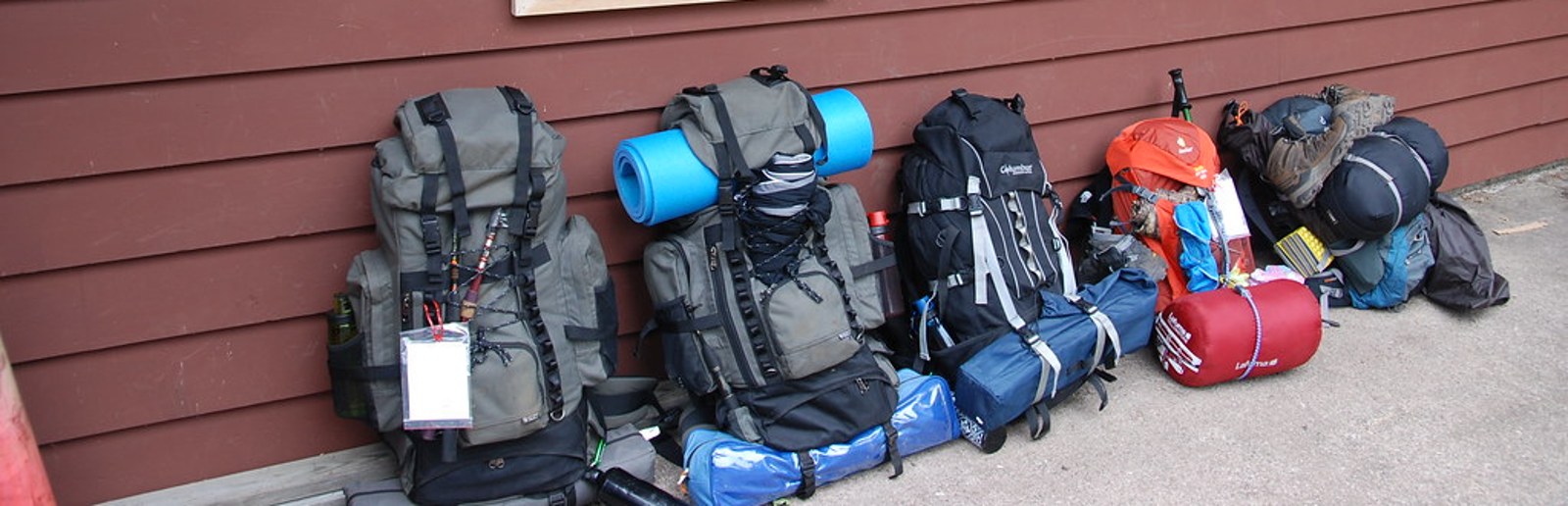 Loaded backpacking packs, sleeping bags, and gear staged outside an outdoor outfitter